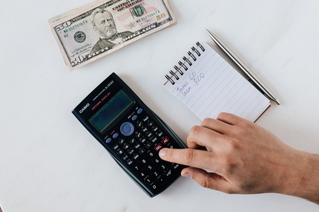 a photo of a hand using a calculator with a small notebook and US dollar note